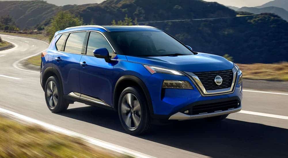 A blue 2021 Nissan Rogue is driving on a winding road.