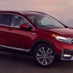 A red 2021 Honda CR-V Touring Hybrid is parked with a city view at sunset after winning the 2021 Honda CR-V vs 2021 Nissan Rogue comparison.