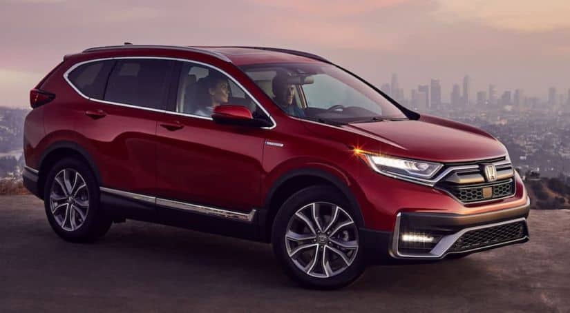 A red 2021 Honda CR-V Touring Hybrid is parked with a city view at sunset after winning the 2021 Honda CR-V vs 2021 Nissan Rogue comparison.