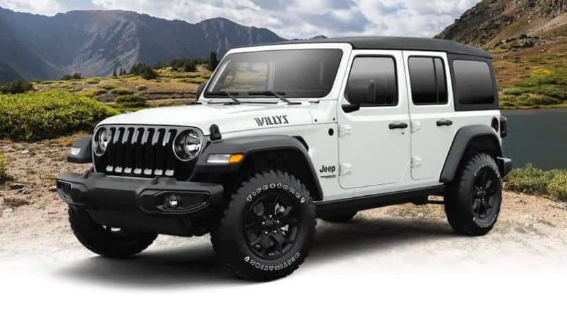 A white 2021 Jeep Wrangler Unlimited Willys is angled left in front of a mountain.