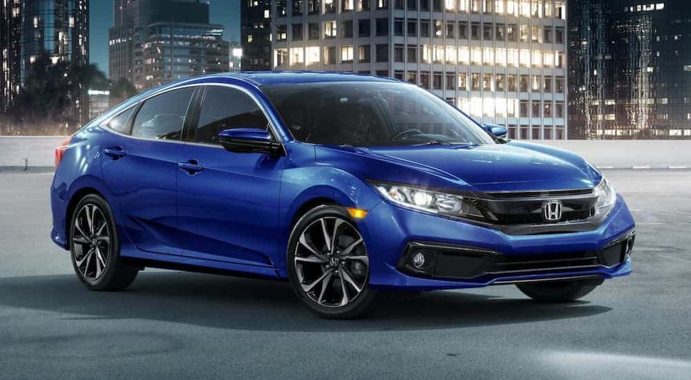 A blue 2021 Honda Civic is parked, angled right, on a parking garage with city buildings in the background.