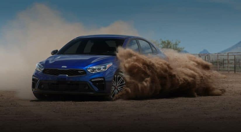 A blue 2021 Kia Forte is driving through the dirt after winning the 2021 Kia Forte vs 2021 Honda Civic comparison.