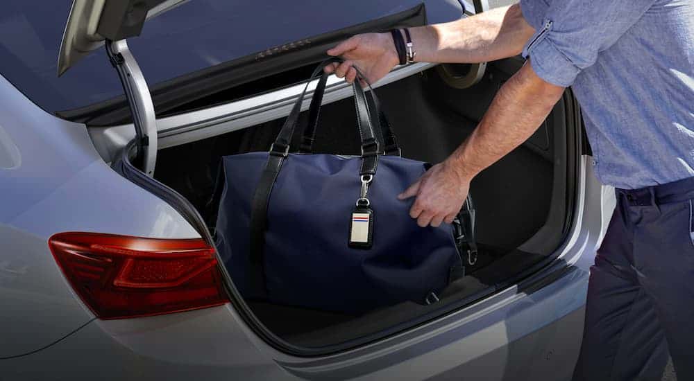 A close up is showing a man loading luggage into the trunk of a silver 2021 Kia Forte.
