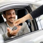 A salesperson is handing keys to a smiling man in a silver car.