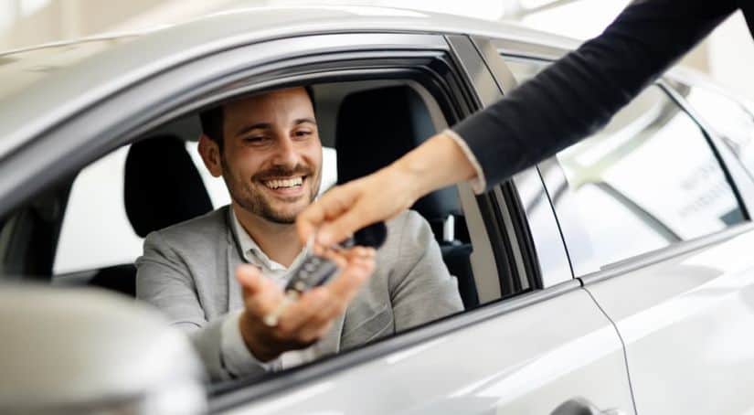 A salesperson is handing keys to a smiling man in a silver car.