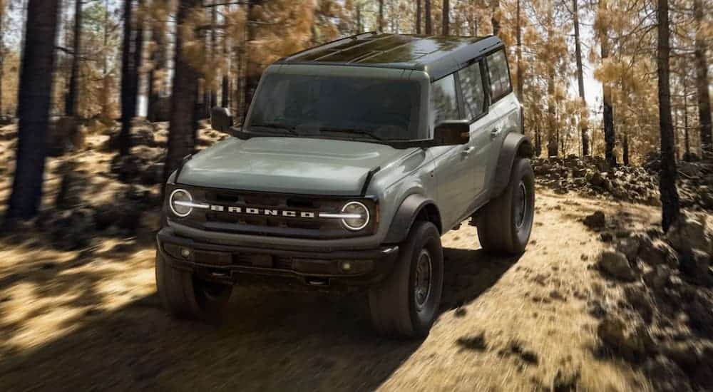 A green 2021 Ford Bronco 4 Door is off-roading on a dirt path in the woods after leaving a car dealer.