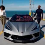 A couple is getting out of a silver 2021 Chevy Corvette Stingray that is parked on a ferry and shown from the front.
