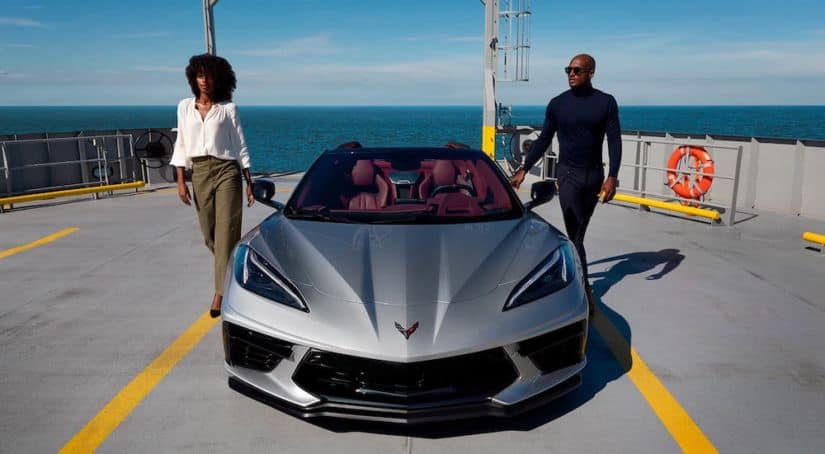 A couple is getting out of a silver 2021 Chevy Corvette Stingray that is parked on a ferry and shown from the front.