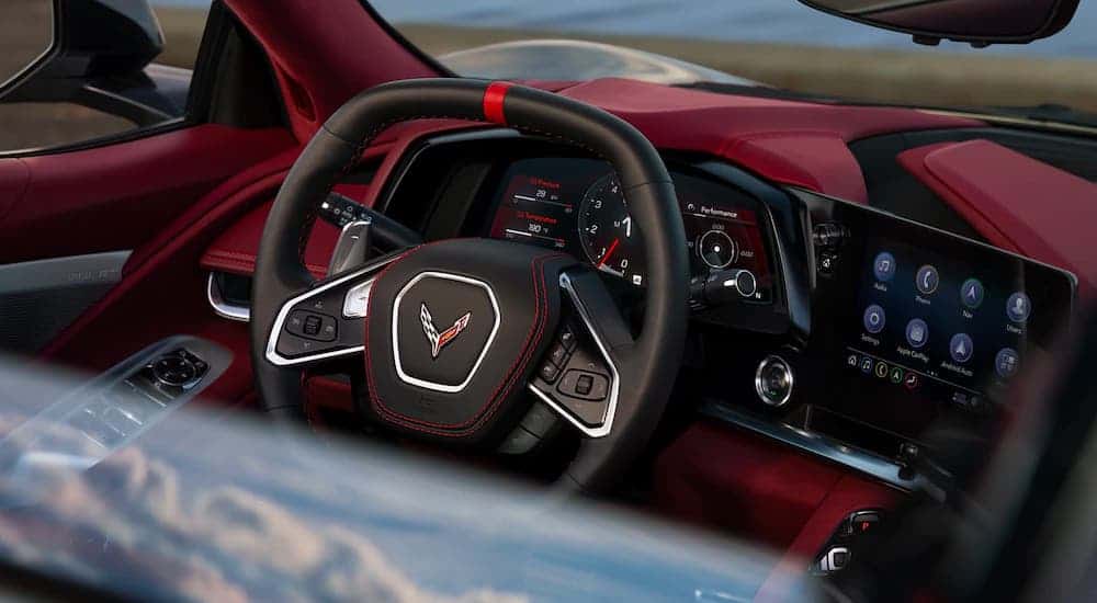 A closeup shows the steering wheel and infotainment screen in a 2021 Chevy Corvette Stingray with a red interior at a local car dealership.