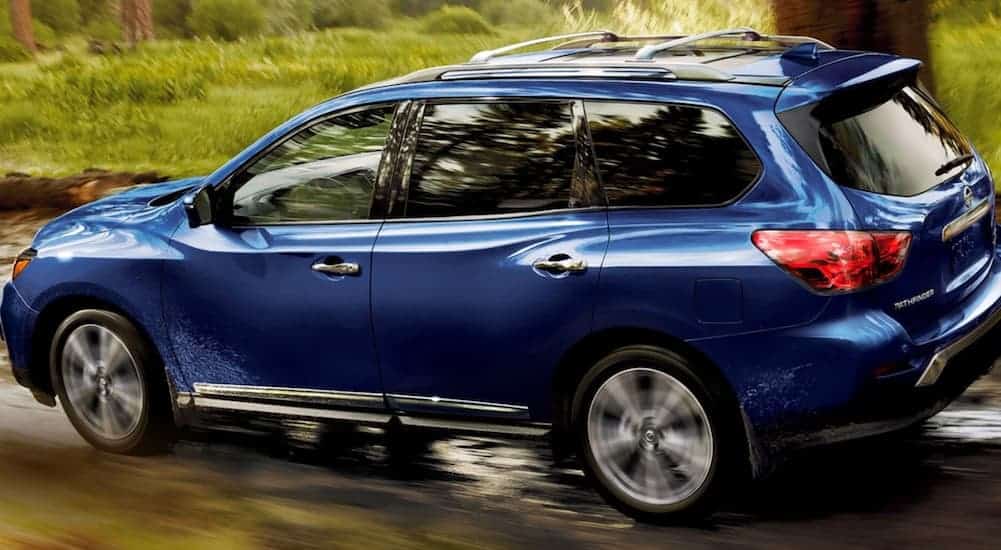 A blue 2020 Nissan Pathfinder is shown from the side driving on a dirt road.