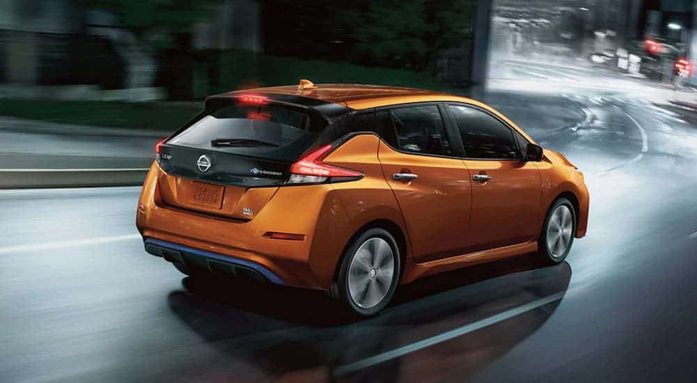 An orange 2021 Nissan LEAF is driving on a city street at night.