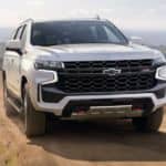 A white 2021 Chevy Tahoe is driving on a dirt road after leaving a Chevy dealer.