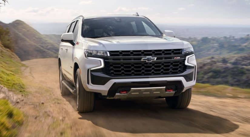 A white 2021 Chevy Tahoe is driving on a dirt road after leaving a Chevy dealer.