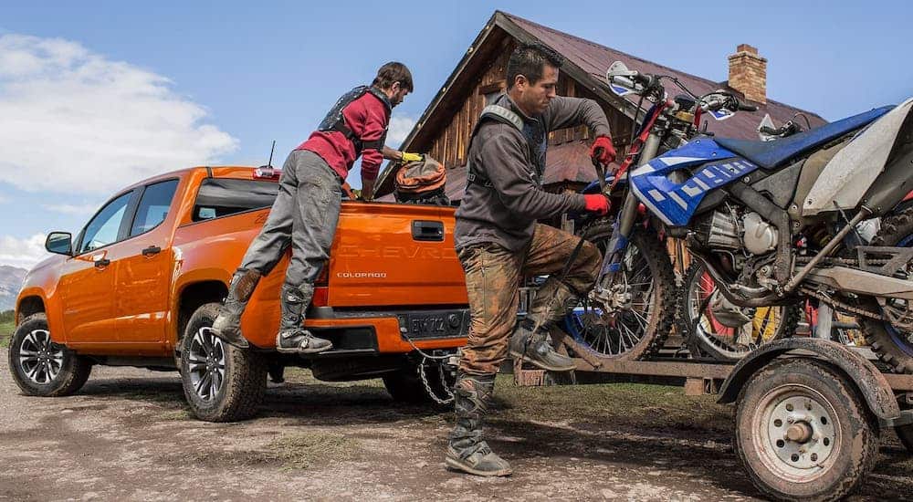 People are loading dirt bikes onto a trailer that is attached to an orange 2021 Chevy Colorado.