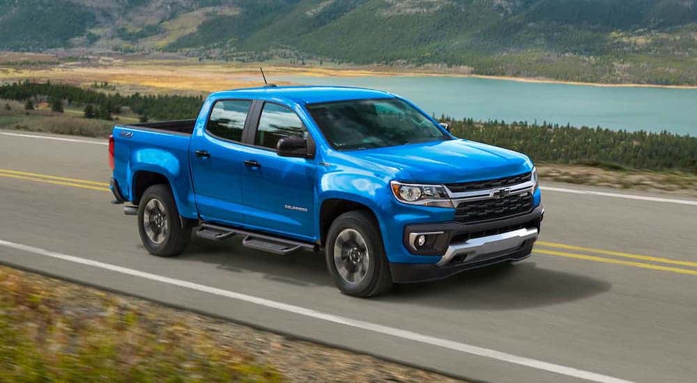 A blue 2021 Chevy Colorado is driving on a highway past hills and a lake after leaving a Chevy truck dealer.