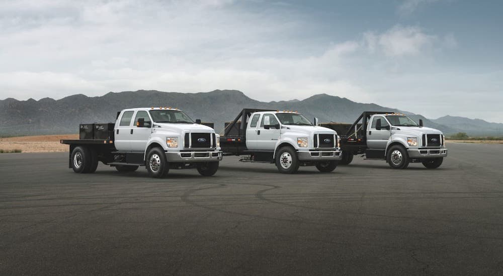 Three white Ford Commercial vehicles are lined up in an empty lot, two of which are 2021 Ford F-650s and a F-750.