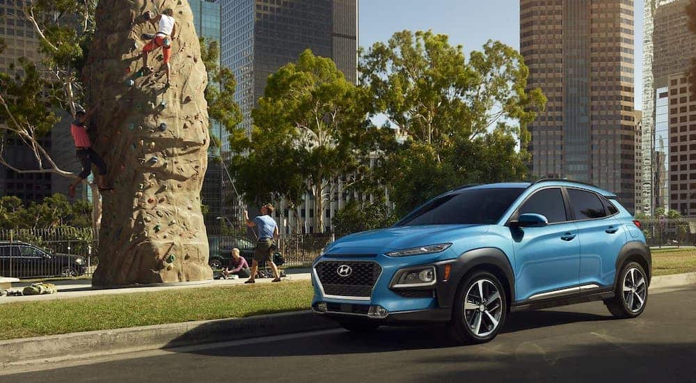 A blue 2021 Hyundai Kona Electric is parked in front of a rock climbing tower.