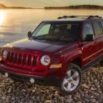 A red 2017 Jeep Patriot is parked on a rocky beach at sunrise.
