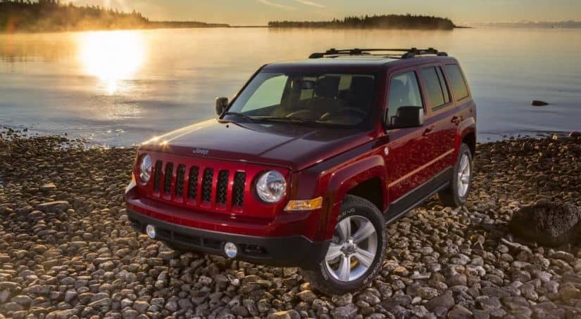 A red 2017 Jeep Patriot is parked on a rocky beach at sunrise.