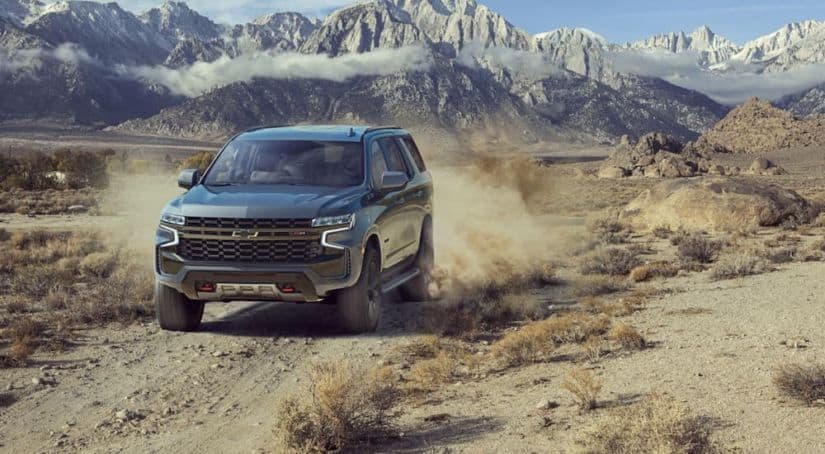 One of our top 10 picks for 2021, a gray 2021 Chevy Tahoe Z71, is driving on a desert road with mountains in the distance.