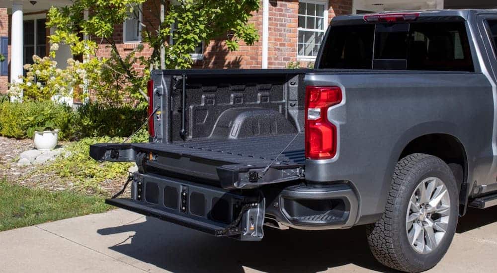 One of the new trucks for sale, a gray 2021 Chevy Silverado 1500, has the Multi-Flex tailgate open while parked in a driveway.