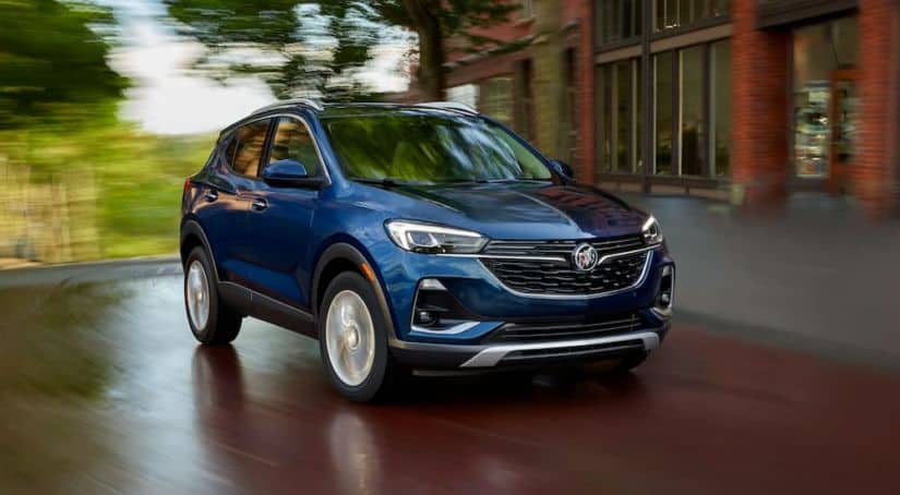 A blue 2020 used Buick Encore GX is driving past a brick building.