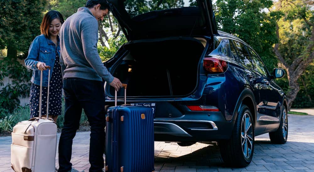 A couple is loading luggage into the back of a blue 2020 Used Buick Encore GX.