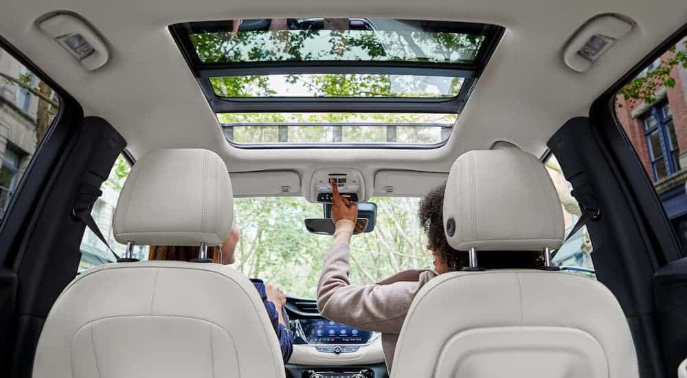 The white interior of a Used Buick Encore GX is shown with a passenger opening the sunroof.