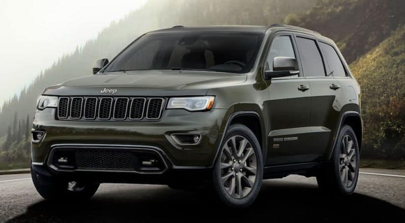 A green 2016 Jeep Grand Cherokee from a used Jeep dealer is parked in front of a mountain.