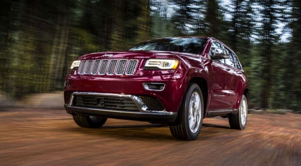 A burgundy 2016 Jeep Grand Cherokee is driving on a dirt road.