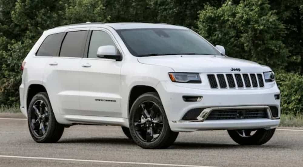 A white 2016 Jeep Grand Cherokee is parked on pavement in front of trees.