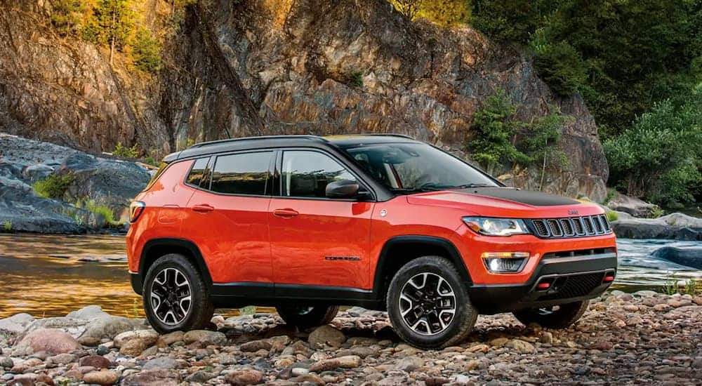A red 2017 Jeep Compass is parked on a rocky river bank.