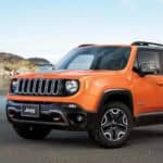 An orange 2018 Jeep Renegade is parked on the sand at a beach with rock formations.