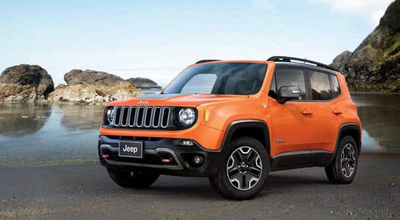 An orange 2018 Jeep Renegade is parked on the sand at a beach with rock formations.