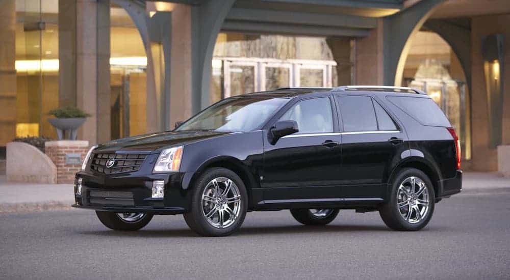 A black 2009 Cadillac SRX, an older used luxury SUV, is parked in front of a modern building.