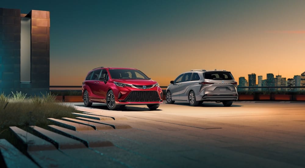 A red and a silver 2019 Toyota Sienna are parked in front of a modern building with a city in the distance.