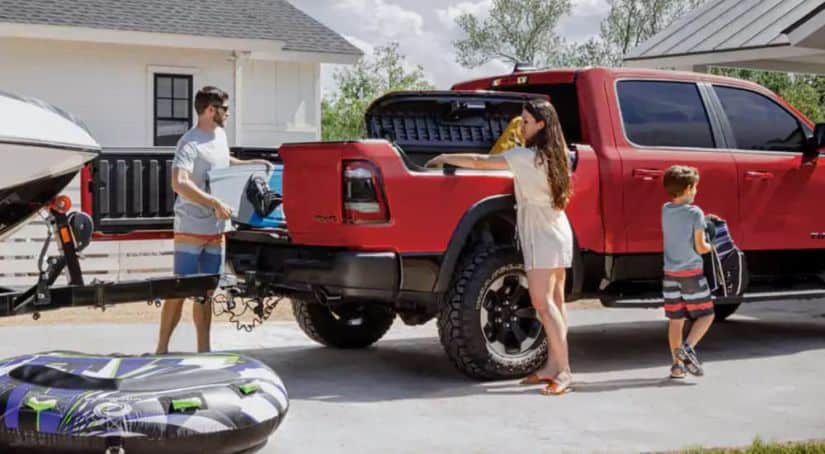 A family is loading tubing and beach gear into a red 2020 Ram 1500, from a used Ram dealer, parked in their driveway.