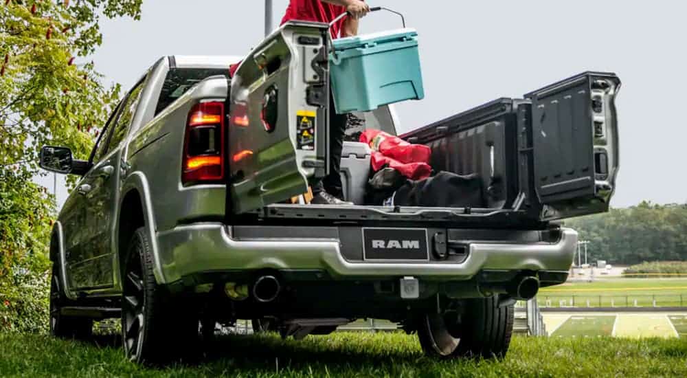 The Multifunction tailgate on a silver 2021 Ram 1500 is shown with a man unloading gear in the bed.