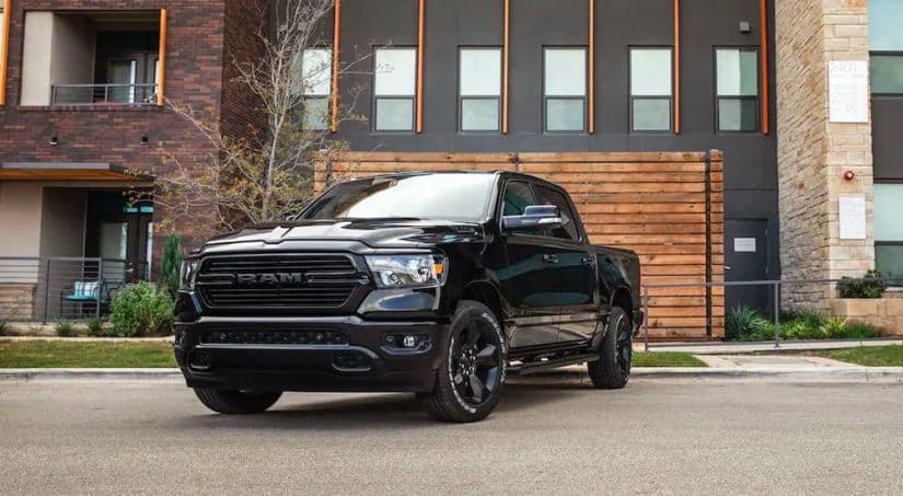 A black 2020 used Ram truck is parked in front of a modern wooden fence and concrete building.