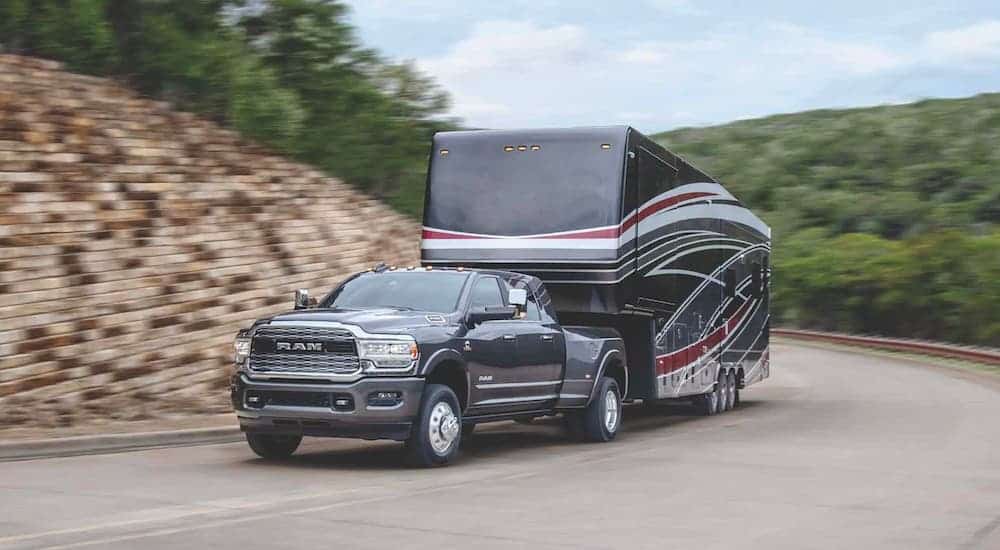 A slate gray 2020 Ram 3500 is towing a large camper on a highway.