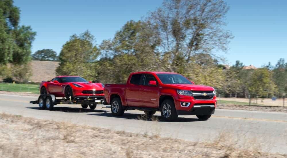 A red 2017 Chevy Colorado is towing a red Corvette down the road.