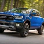 A popular used truck in DFW, a blue 2019 Ford Ranger, is driving down the road past blurred trees.