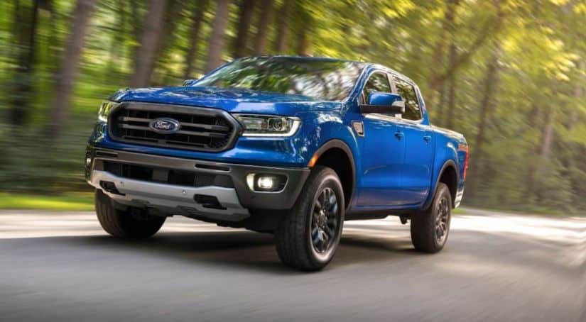 A popular used truck in DFW, a blue 2019 Ford Ranger, is driving down the road past blurred trees.