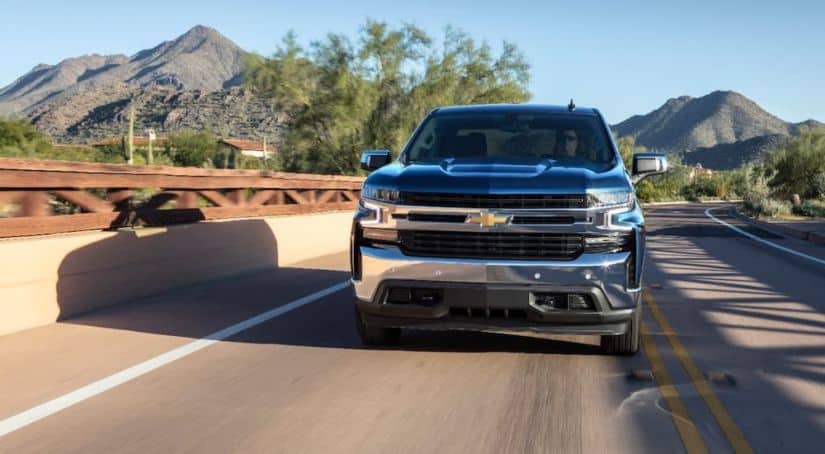 A popular used truck for sale, a blue 2019 Chevy Silverado, is shown from the front on a highway with a mountain in the distance.
