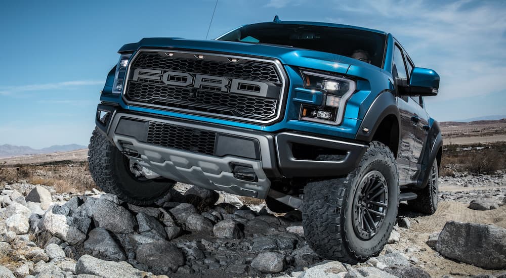 A blue 2020 Ford F-150 Raptor is shown from the front parked on a rocky path.