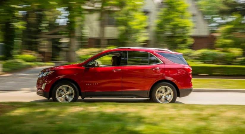 A red 2021 Chevy Equinox is shown from the side driving on a suburban street.