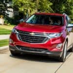 A red 2021 Chevy Equinox is driving on a suburban road after winning the 2021 Chevy Equinox vs 2021 Honda CR-V comparison.