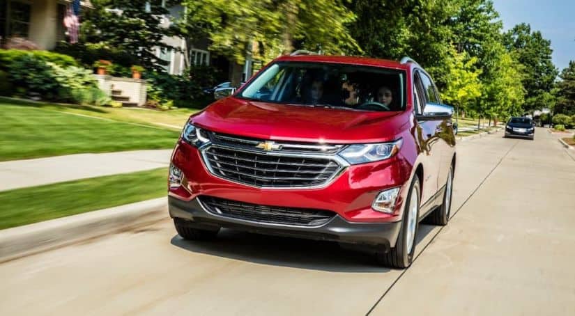A red 2021 Chevy Equinox is driving on a suburban road after winning the 2021 Chevy Equinox vs 2021 Honda CR-V comparison.