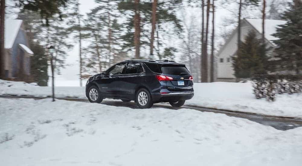 A blue 2021 Chevy Equinox is shown from a rear angle while driving on a snowy road.