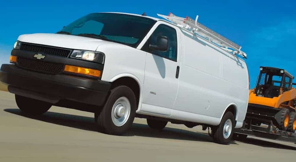 A white 2021 Chevy Express Van is towing construction equipment on a highway.